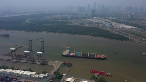 Vista-Aérea-Del-Río-Saigón-Con-La-Instalación-Portuaria-De-Aguas-Profundas,-El-Transporte-Marítimo,-Los-Humedales-Y-Elementos-Del-Horizonte-De-La-Ciudad-En-Un-Día-De-Alta-Contaminación-Del-Aire