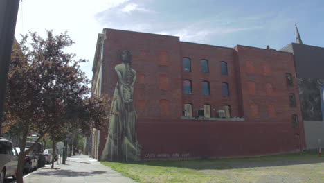 People-walking-past-large-wall-art-of-young-girl-in-a-dressed-with-her-back-turned-downtown-Portland,-Oregon,-USA