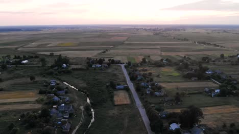 Aerial-View-of-Small-Farm-Town-With-Houses-and-one-Road-at-Dusk-With-Fields-in-Background