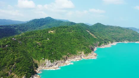 Shiny-turquoise-sea-washing-rocky-coastline-of-beautiful-tropical-island-with-lush-vegetation-of-green-hills-in-Thailand