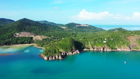 Laguna-Tranquila-Y-Colorida-Que-Lava-La-Hermosa-Costa-Rocosa-De-Una-Isla-Tropical-Con-Colinas-Verdes-En-Un-Cielo-Brillante-Con-Fondo-De-Nubes-Blancas-En-Koh-Phangan,-Tailandia