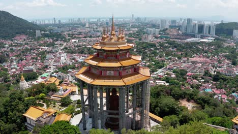 Aerial-view-of-the-city-and-Kek-Lok-Si-Buddhist-temple-with-Kuan-Yin-statue-shrine-visible,-Drone-back-view-wide-pan-left-shot