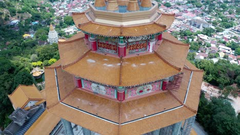 Aerial-back-view-of-Kuan-Yin-statue-shrine-and-Kek-Lok-Si-Buddhist-temple-with-the-city-in-the-background,-Drone-orbit-left-reveal-shot