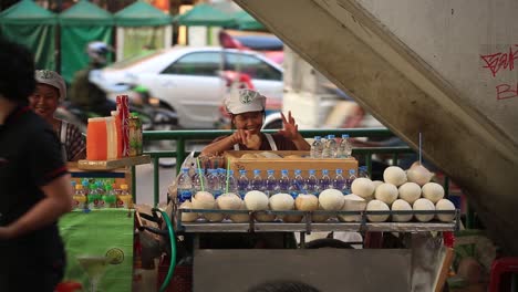 Bangkok,-Thailand---Straßenhändler,-Die-Speisen-Und-Getränke-Im-Pratunam-Gebiet-Verkaufen,-Mit-Vorbeifahrenden-Transportfahrzeugen-Im-Hintergrund---Nahaufnahme