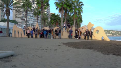 Tourists-pose-for-a-photo-on-Malagueta-beach-with-palm-trees-and-skyscrapers-on-the-background,-Malaga,-Spain