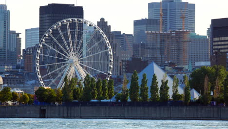 Ferris-Wheel-close-up-view,-old-port-Montreal,-Pyramid-PY,-river,-cityscape-panorama,-buildings,-skyscrapers,-construction,-boat-passing