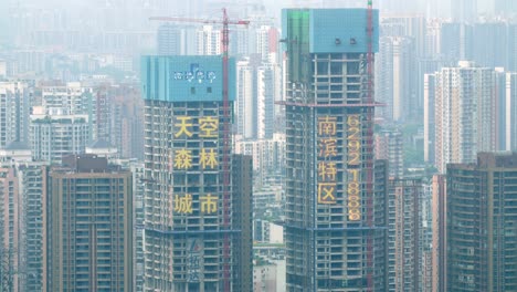 Edificios-Gemelos-En-Construcción-Con-Grúas-Rojas-Con-Retenedores-De-Hormigón-Y-Que-Muestran-La-Ciudad-Con-Neblina-De-Contaminación-Del-Aire,-Tiro-De-Establecimiento-Bloqueado