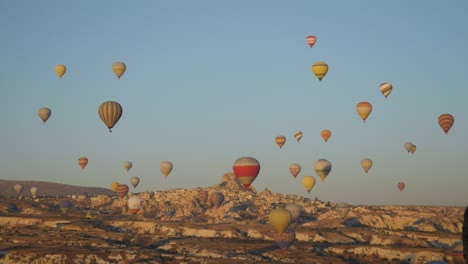 Sky-filled-with-hot-air-balloons-drifting-over-the-dry-landscape-of-Cappadocia,-Turkey
