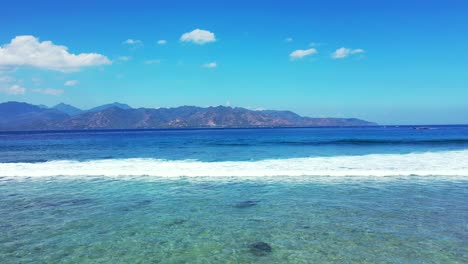 Weiße-Wellen-Aus-Tiefblauem-Meer,-Die-über-Felsen-Und-Korallenriffe-Am-Ufer-Schäumen,-Mit-Ruhigem,-Flachem-Wasser-Auf-Einem-Strahlend-Blauen-Himmelshintergrund-In-Malaysia