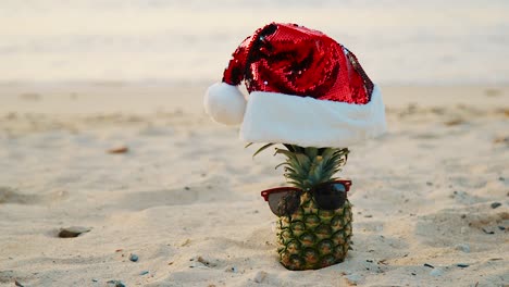 Strand-Auf-Curaçao-–-Ananas-Mit-Roter-Weihnachtsmütze-Und-Sonnenbrille-Am-Sandstrand-Mit-Wellen-Im-Hintergrund-–-Nahaufnahme