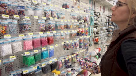 Over-the-shoulder-shot-of-blonde-woman-looking-at-packages-of-multicolored-beads-in-a-craft-store