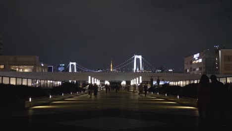 Nachtszene-Des-Odaiba-Gehwegs-Mit-Vorbeigehenden-Menschen-Und-Der-Regenbogenbrücke-In-Der-Bucht-Von-Tokio-Im-Hintergrund,-Tokio,-Japan