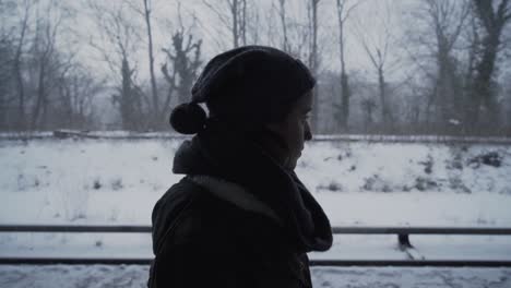 Woman-standing-outside-in-winter-hat-and-scarf-watching-snow