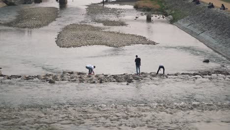 Tres-Hombres-Cruzando-Los-Escalones-Y-Jugando-En-El-Agua-En-El-Río-Kamogawa-En-Kyoto,-Japón