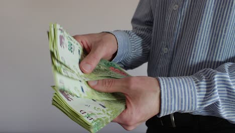 Young-businessman-counting-Argentine-cash-money-"pesos".-Close-up