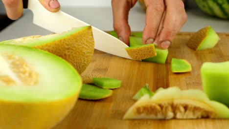 Slicing-Galia-melon-into-chunks,-using-a-ceramic-knife,-on-a-bamboo-cutting-board