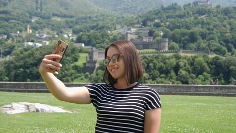 Woman-taking-selfy-picture-of-herself,-castle-background-warm-wind-blowing,-small-village-town-Switzerland