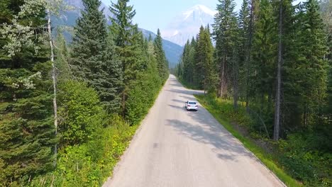 White-car-driving-on-a-road-in-the-middle-of-a-forest-in-the-mountains,-aerial-drone-shot