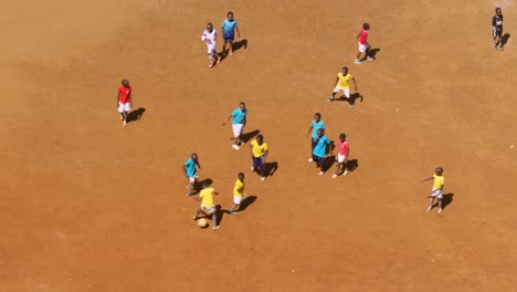 Niños-Jugando-Al-Fútbol-En-Un-Campo-De-Tierra-Roja-En-Nairobi-Con-Ropa-Brillante-En-Cámara-Lenta