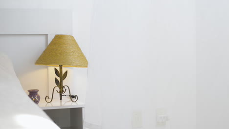 Bedside-lamp-on-a-bedside-table-with-the-curtain-moving-because-of-the-wind