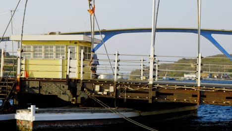 Hombre-Caminando-En-El-Puente-De-La-Reina-Emma-Y-Pasando-Por-La-Casa-De-Control-En-Punda,-Curacao