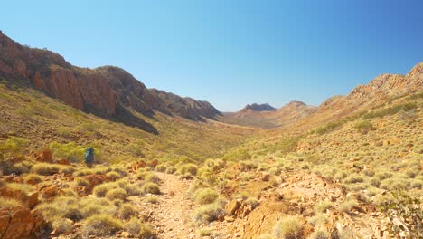 Hiker-walks-through-desert-valley-between-mountain-ridges,-Australia