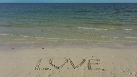 Wide-angle-shot-of-LOVE-inscribed-in-the-sand-with-emerald-and-blue-water-on-the-horizon
