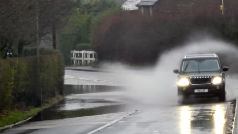 Land-Rover-Spritzt-Auf-Große-Welle,-Die-Auf-Einer-Stürmischen,-Von-Sturzfluten-überschwemmten-Straße-In-Einer-Kurve-In-Großbritannien-Fährt