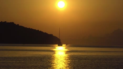 Sunset-at-Vela-Luka,-Croatia,-with-a-sailboat-and-motorboat-traveling-across-the-view