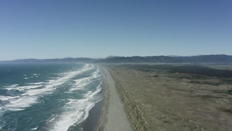 Wide-drone-shot-of-southern-Oregon-coast,-blue-waves-coming-into-shore