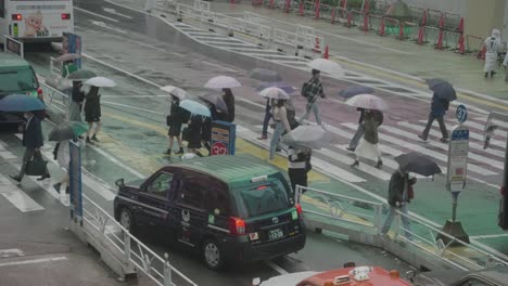 Pedestrians-With-Umbrellas-On-A-Rainy-Day-Crossing-The-Road-With-A-Taxi-Stand-In-Shibuya,-Tokyo,-Japan