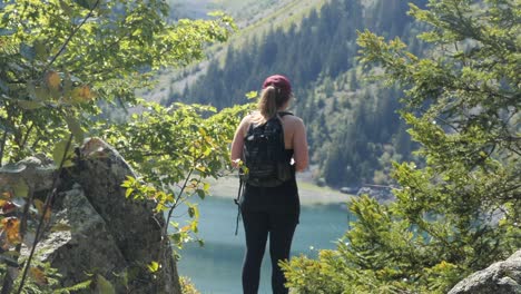 Gorgeous-wide-shot-of-an-attractive-young-woman-enjoying-the-view-of-clear-lake-in-the-alps-of-Venosc,-France