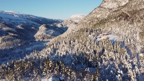 Weite-Offene,-Atemberaubende,-Verträumte-Winterlandschaft,-Luftaufnahmen,-Die-Sich-Rückwärts-Vom-Berg-Bewegen-Und-Einen-Abgelegenen-Bauernhof-Im-Winterwald-Offenbaren