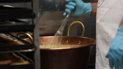 Baker-Wearing-A-Blue-Gloves,-Stirring-Using-Egg-Whisk-On-A-Deep-Copper-Pan