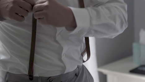 Groom-adjusting-his-suspenders-morning-of-wedding