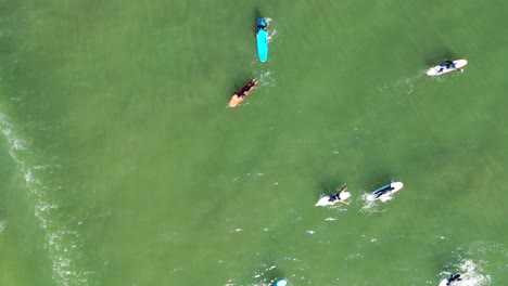 A-top-down-drone-shot-over-surfers-waiting-for-a-wave-which-rolls-in---sprays-a-beautiful-mist