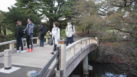 Menschen-An-Der-Hölzernen-Fußgängerbrücke-Tragen-Gesichtsmaske-Aufgrund-Einer-Pandemie-Im-Nationalgarten-Shinjuku-Gyoen,-Tokio,-Japan