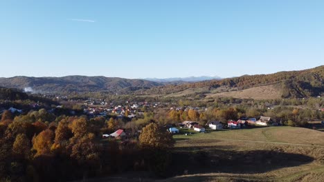 Luftaufnahme-über-Dem-Epischen-Bunten-Herbstwald-Und-Einem-Ländlichen-Dorf-An-Einem-Sonnigen-Tag