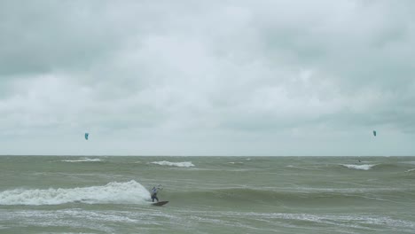 Kite-surfing-surfers-sailing-on-the-big-Baltic-sea-waves-at-Liepaja-Karosta-beach,-overcast-autumn-day,-slow-motion-wide-shot