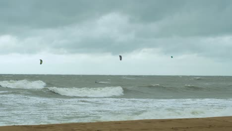 Kite-surfing-surfers-sailing-on-the-big-Baltic-sea-waves-at-Liepaja-Karosta-beach,-overcast-autumn-day,-wide-shot