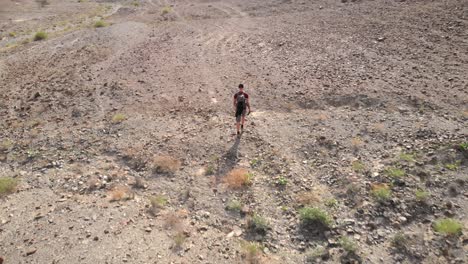 Aerial-tracking-shot-from-drone-of-an-young-male-walking-in-a-rocky-desert-valleys-in-Hatta,-United-Arab-Emirates