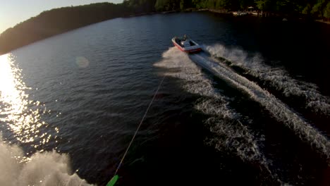 Super-Slow-Motion---White-Man-Slalom-Water-Skis-behind-Boat-on-Blue-Lake-in-Summer-Sunset-Light,-FPV-Drone-Aerial-Tracking