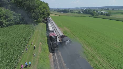 Aerial-View-of-a-1910-Steam-Engine-with-Passenger-Train-Puffing-Smoke-Traveling-Along-the-Amish-Countryside-as-a-Second-Steam-Train-Passes-on-a-Sunny-Summer-Day-as-Seen-by-a-Drone