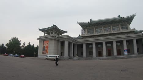 Hombre-Norcoreano-Camina-Frente-Al-Gran-Teatro-De-Pyongyang,-Corea-Del-Norte