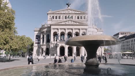 Old-Opera-house-with-water-fountain-and-people-as-forefront-in-Frankfurt,-Germany