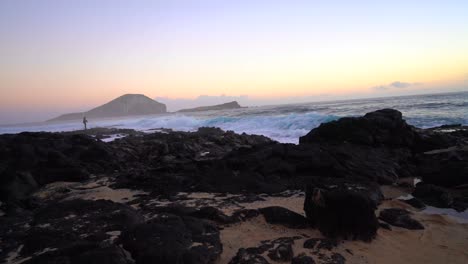 High-tide-rushing-over-the-tide-pools-of-Makapuu-Beach-at-sunrise-with-a-photographer-holding-a-camera-in-the-far-distance