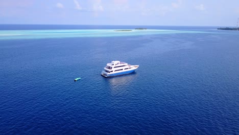 Ferry-approaching-slowly-toward-seashore-of-tropical-island-in-the-middle-of-deep-blue-ocean-surrounded-by-shallow-turquoise-waters-of-Maldives