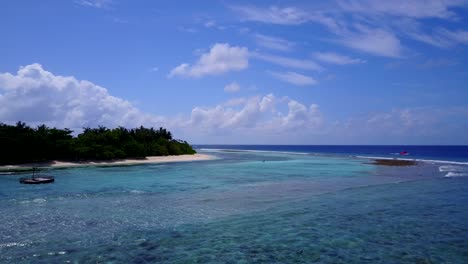 Lebendige-Farben-Der-Blauen-Azurblauen-Lagune-Mit-Weißen-Wellen,-Die-Den-Exotischen-Strand-Unter-Der-üppigen-Vegetation-Der-Insel-Und-Den-Hellblauen-Himmel-Mit-Weißen-Wolken-Auf-Den-Bahamas-Umspülen