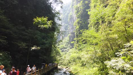 Zhangjiajie,-China---August-2019-:-Tourists-walking-on-the-scenic-pathway-along-the-narrow-river-flowing-through-the-majestic-Grand-Canyon-in-Zhangjiajie-National-Park