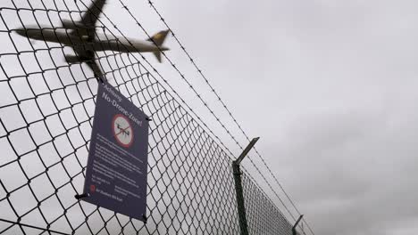 Drones-forbidden-sign-at-frankfurt,-germany-airport-fence-next-to-highway-a5-with-aircraft-airplane-passing